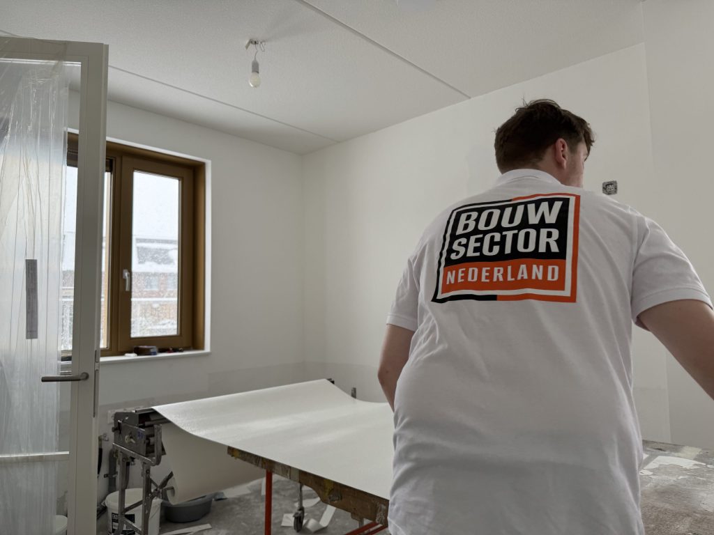 Behanger van Bouwsector Nederland legt een baan vlies klaar op de plaktafel in een lege kamer