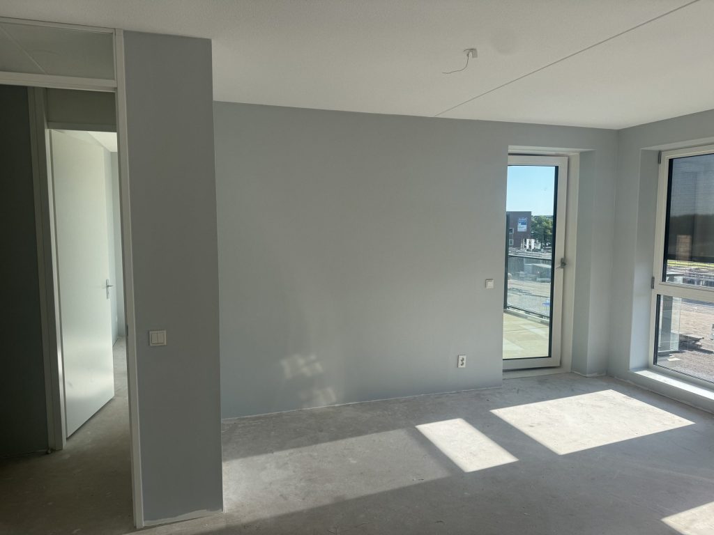 Nieuw appartement met lichtgrijze wanden, een balkondeur en een kale betonvloer
