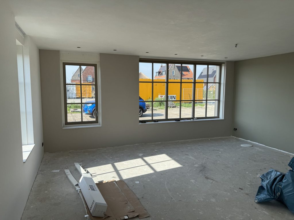 Woonkamer in een nieuwbouwwoning met grote ramen en wanden in een warme grijstint