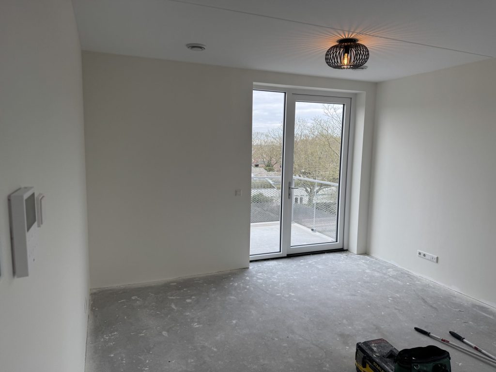 Lichte kamer in een appartement met witte wanden en een deur naar het balkon