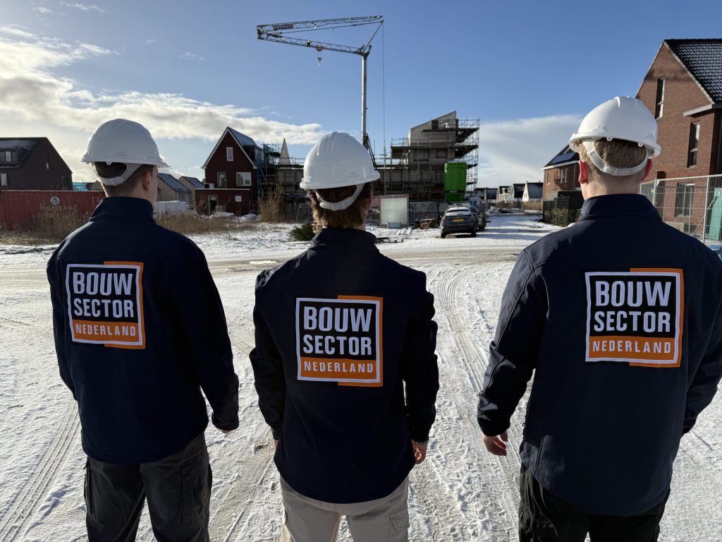 Drie vakmensen van Bouwsector Nederland met witte helm kijken naar woningen in aanbouw